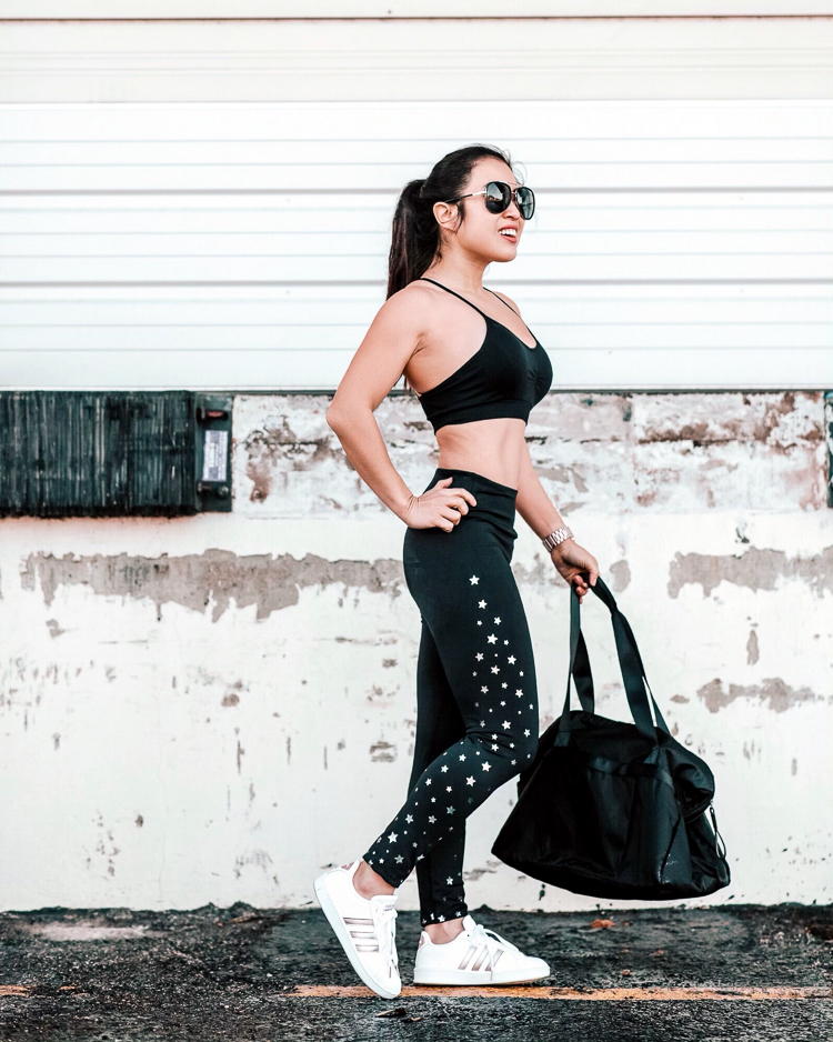 JCPenney Activewear featured by top US petite fashion blog Cute & Little; Image of a woman wearing jcpenney xersion strappy bra, star print leggings, adidas advantage white stripe sneakers, gaiam yoga gym bag and quay needing fame aviator sunglasses