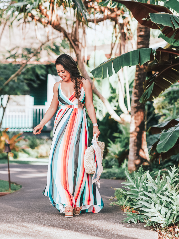 cute & little | popular petite dallas fashion blog | express striped surplice front lace-up back maxi dress | tropical beach vacation outfit | A Tropical Maxi Dress for your Next Beach Vacation by popular Dallas blog Cute and Little: image of woman standing outside by palm trees and wearing a Express Stripe Surplice Lace-Up Maxi, See By Chloe 'Glyn' Espadrilles, and holding an Amazon Straw Tote with a  Red Dress Boutique Scarf tied to handles of the purse.
