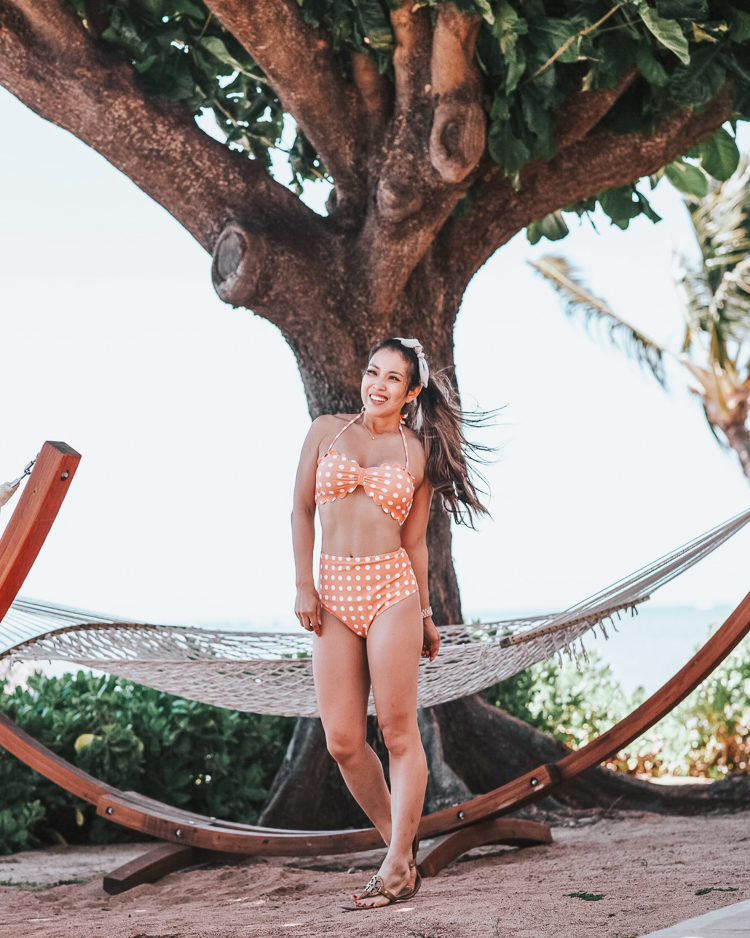 cute & little | popular dallas petite fashion travel blog | amazon cupshe high-waisted mom friendly peach scallop bikini | molokai maui beach | Affordable Fashion: Cute Summer Swimsuits you Need by popular Dallas blog Cute and Little: Image of a woman in Maui, Hawaii standing outside in front of a hammock under a tree and wearing a Amazon Cupshe Peach Polka Dot Bikini, Baublebar 'Brianna' Heart Hoops, Amazon Striped Knot Headband, Etsy Solitaire 15" necklace, Fitbit 'Versa' smartwatch and Tori Burch Miller sandals. 