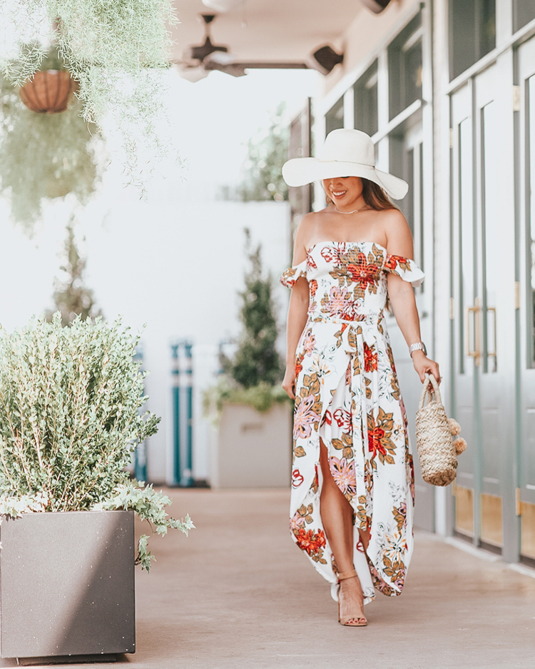 cute & little blog | popular dallas petite fashion blog | walmart we dress america summer outfit | floral off-shoulder maxi dress, wide straw floppy hat, straw pom pom tote bag | beach vacation outfit | 3 Summer Trends you Need to Try this Season featured by top US petite fashion blog, cute & little: image of a woman wearing a New Look maxi floral dress, Eliza May Rose straw sunhat, Eliza May Rose mini tote, TrendsBlue necklace, Report Ankle High Heels, Fitbit and Versa Smartwatch.