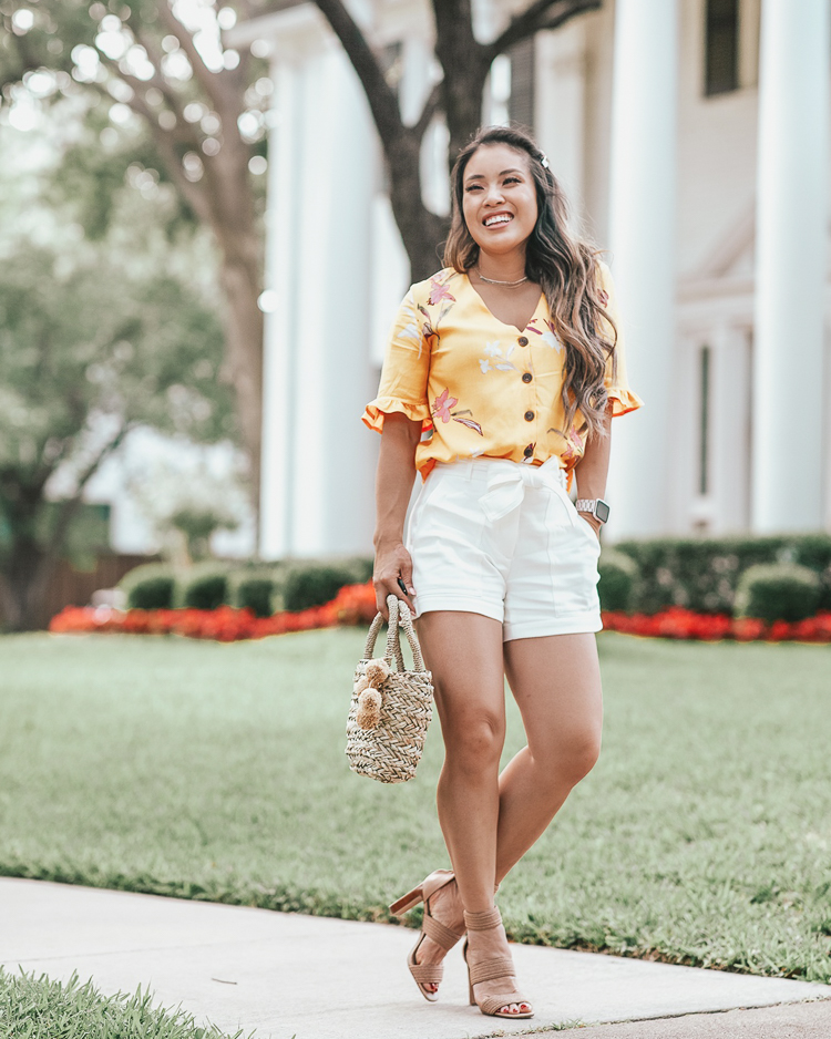 Ann Taylor Cyber Sale featured by top US petite fashion blog Cute & Little; Image of a woman wearing walmart fashion yellow floral ruffle blouse, ann taylor marina tie waist white shorts, steve madden jelly nude strappy sandals and walmart eliza may rose straw pom pom bag.