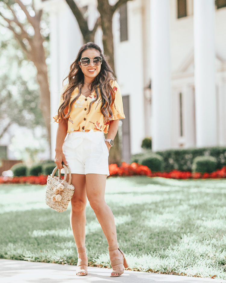 Ann Taylor Cyber Sale featured by top US petite fashion blog Cute & Little; Image of a woman wearing walmart fashion yellow floral ruffle blouse, ann taylor marina tie waist white shorts, steve madden jelly nude strappy sandals and walmart eliza may rose straw pom pom bag.