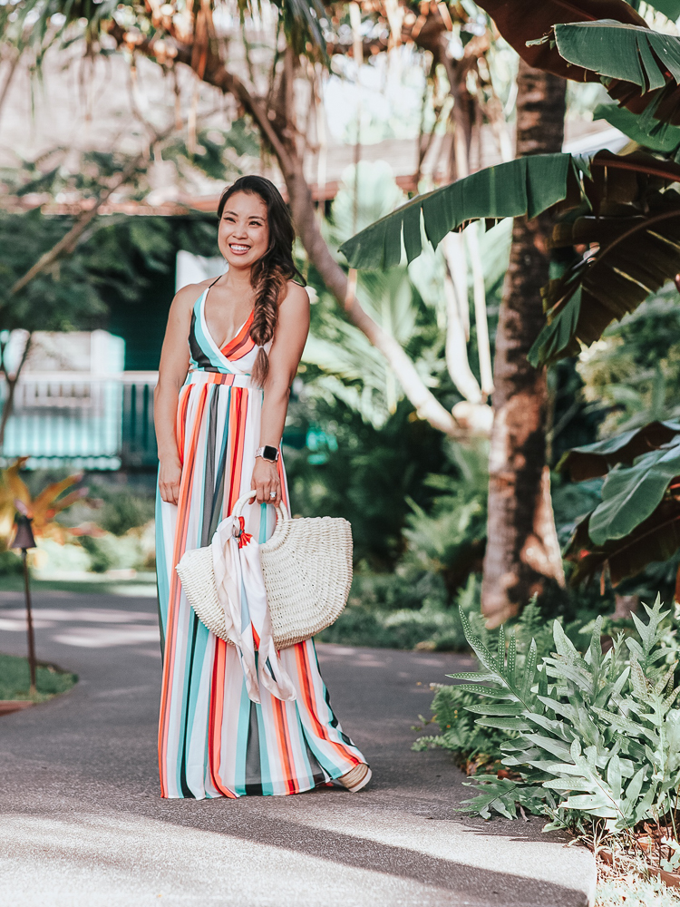 cute & little | popular petite dallas fashion blog | express striped surplice front lace-up back maxi dress | tropical beach vacation outfit | A Tropical Maxi Dress for your Next Beach Vacation by popular Dallas blog Cute and Little: image of woman standing outside by palm trees and wearing a Express Stripe Surplice Lace-Up Maxi, See By Chloe 'Glyn' Espadrilles, and holding an Amazon Straw Tote with a  Red Dress Boutique Scarf tied to handles of the purse.