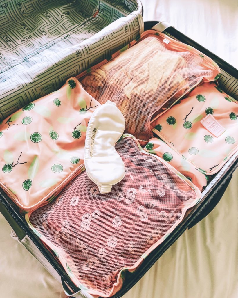 cute & little | popular dallas travel blog | how to organize luggage | best travel packing cubes | amazon travel must-have essential | 5 Ways I Save Money On Travel by popular Dallas travel blog, Cute and Little: image of an open suitcase on a bed with citrus packing bags and a white sleep mask.