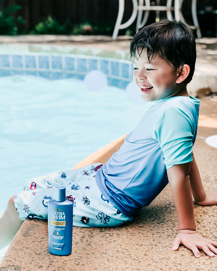 cute & little | popular dallas fashion blog | ultra swim hair care | summer adventure vacation essentials | 4 Essentials For The Family Summer Vacation Packing List by popular Dallas petite fashion blog, Cute and Little: image of a boy sitting at the edge of a pool with a bottle of 