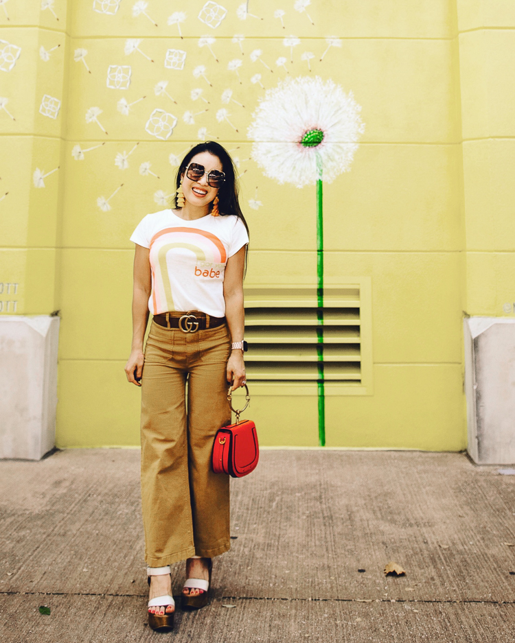 cute & little | popular dallas fashion blog | dallas mural guide | instagram walls | kendra scott dandelion yellow wall | west village uptown | Dallas Mural Guide: Top 10 Instagram Walls by popular Dallas blog, Cute and Little: image of a woman standing in front of a Dandelion mural and wearing a rainbow tee, J. Crew Point Sur washed wide-leg crop pant, Amazon Yoome Women Punk Circular Ring Handle Handbags Small Round Purse Crossbody Bag, and Gucci GG 0106 S- GG0106S Sunglasses.