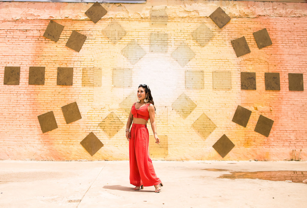 cute & little | popular dallas fashion blog | dallas mural guide | instagram walls | sun rays wall | deep ellum | Dallas Mural Guide: Top 10 Instagram Walls by popular Dallas blog, Cute and Little: image of a woman standing in front of a sun rays mural and wearing red wide leg pants, a red crop tie top, and Sam Edelman sandals.