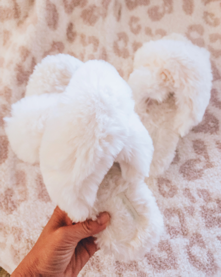 cute & little | august 2019 top sellers | amazon white fuzzy criss cross house lounge slippers | August 2019 Top Sellers by popular Dallas petit fashion blog, Cute and Little: image of a woman holding a pair of Women's Cross Band Soft Plush Fleece House/Outdoor Slippers.