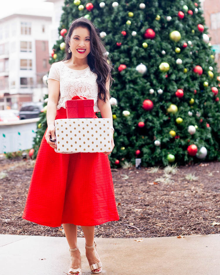 cute & little | dallas petite fashion blog | holiday christmas festive outfit | red midi skirt | The Best After Christmas Sales 2019 by popular Dallas fashion blog, Cute and Little: image of a woman holding wrapped presents in front of a Christmas tree and wearing a lace top, red midi skirt, sandals, and ARMANI BEAUTY Lip Maestro Liquid Lipstick.