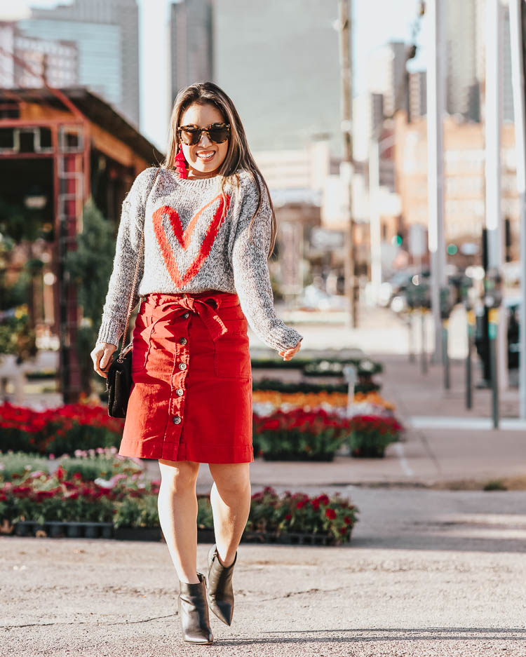 cute & little | dallas petite fashion blog | loft red heart print grey sweater, red button skirt | valentines day work business casual outfit | Heart Print Fashion For Valentine's Day And Later by popular Dallas petite fashion blog, Cute and Little: image of a woman wearing a Loft HEART SWEATER, Loft TIE WAIST BUTTON FRONT SKIRT and Marc Fisher Mella booties.