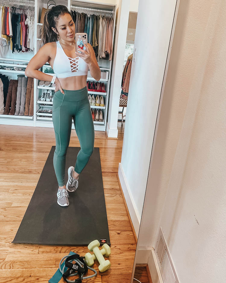 cute & little | dallas fitness lifestyle blogger | at home workouts | Best Online Home Workouts by popular Dallas lifestyle blog, Cute and Little: image of a woman standing on a yoga mat next to some hand weights and wearing a Forever 21 bralette, Lululemon Invigorate High-Rise Tight 25", and DSW QT RACER SNEAKER. 