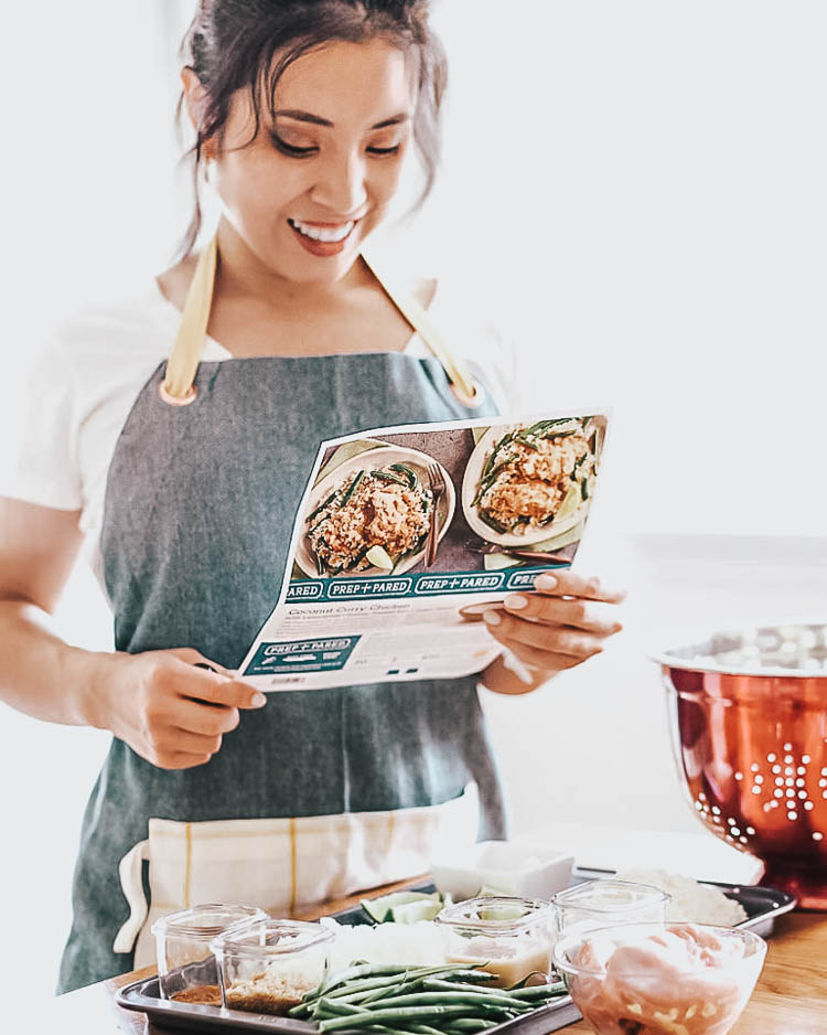comparing 5 different home meal delivery kits | best meal delivery kit | Meal Delivery Service Reviews by popular Dallas lifestyle blog, Cute and Little: image of a woman wearing a grey apron and holding a Home Chef recipe sheet. 