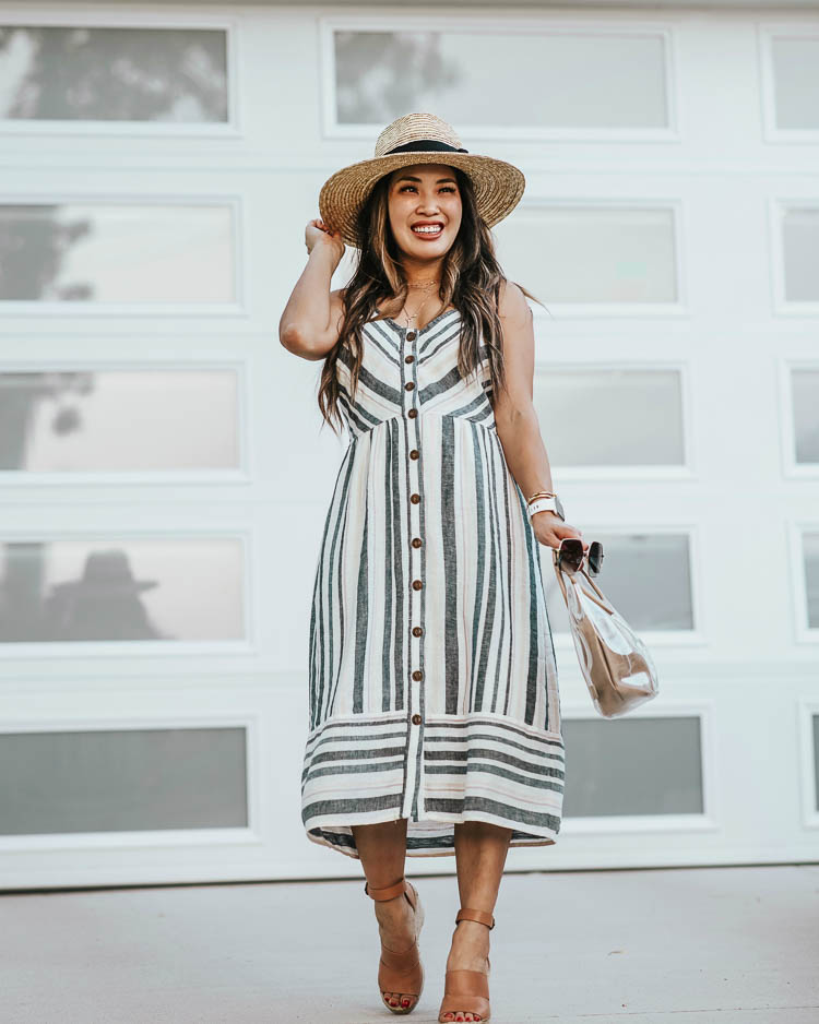 cute & little | target summer dresses | striped midi dress, brixton straw hat | Target Summer Dresses by popular Dallas petite fashion blog, Cute and Little: image of a woman standing outside and wearing a Target Target Universal Thread Button-Front Sun Dress, Treasure & Bond ‘Sannibel’, Fitbit ‘Versa’ Lite, Panacea Layered Circle Pendant, Brixton ‘Joanna’ Straw Hat, Quay ‘Backstage’ sunglasses, and holding an amazon clear tote bag. 