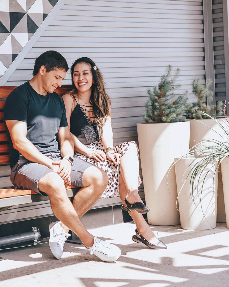 cute & little blog | fathers day amazon gift guide | Father's Day Gift Ideas by popular Dallas lifestyle blog, Cute and Little: image of a man and woman sitting together outside on a wooden bench and wearing a wayf posie cami, leopard midi skirt, black studded flats, star hair clip, crew shirt, grey khaki shorts, and white/tan sneaker.