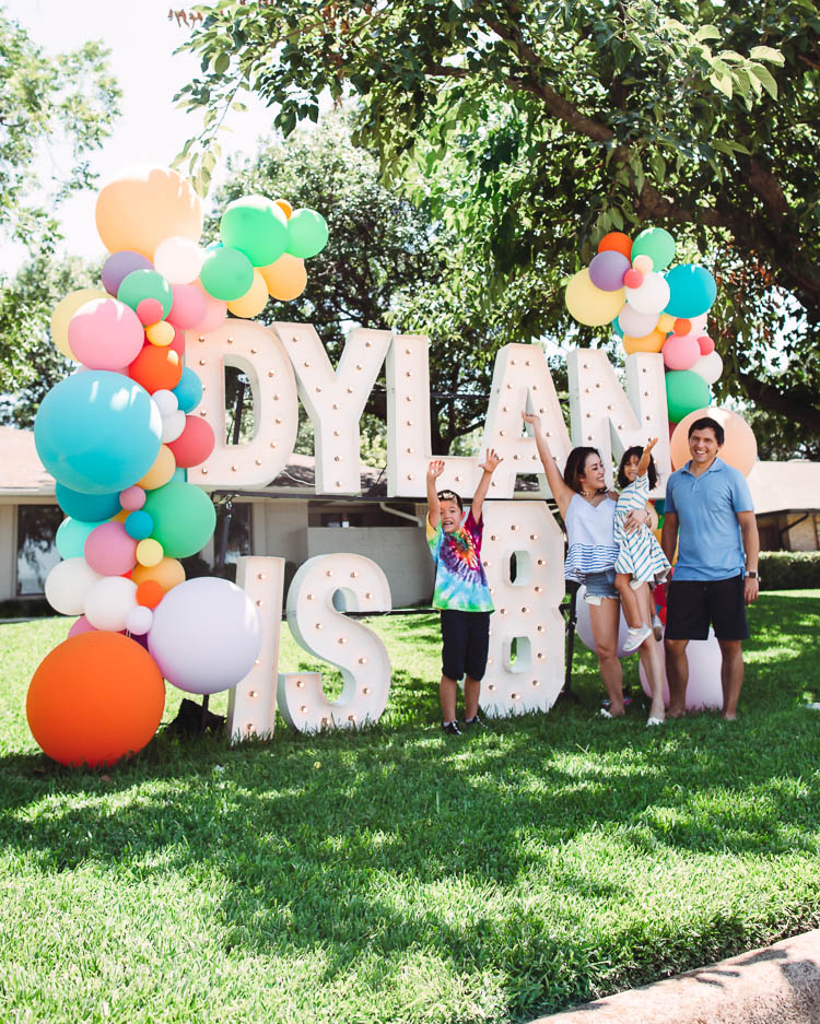 cute & little | dallas fashion lifestyle blog | quarantine social distancing kids birthday party ideas | lushra DIY balloon garland | Birthday Party Ideas for Kids by popular Dallas lifestyle blog, Cute and Little: Pinterest image of a family standing in front of a Alpha-LIt Marquee letters sign and Lushra balloon garland.