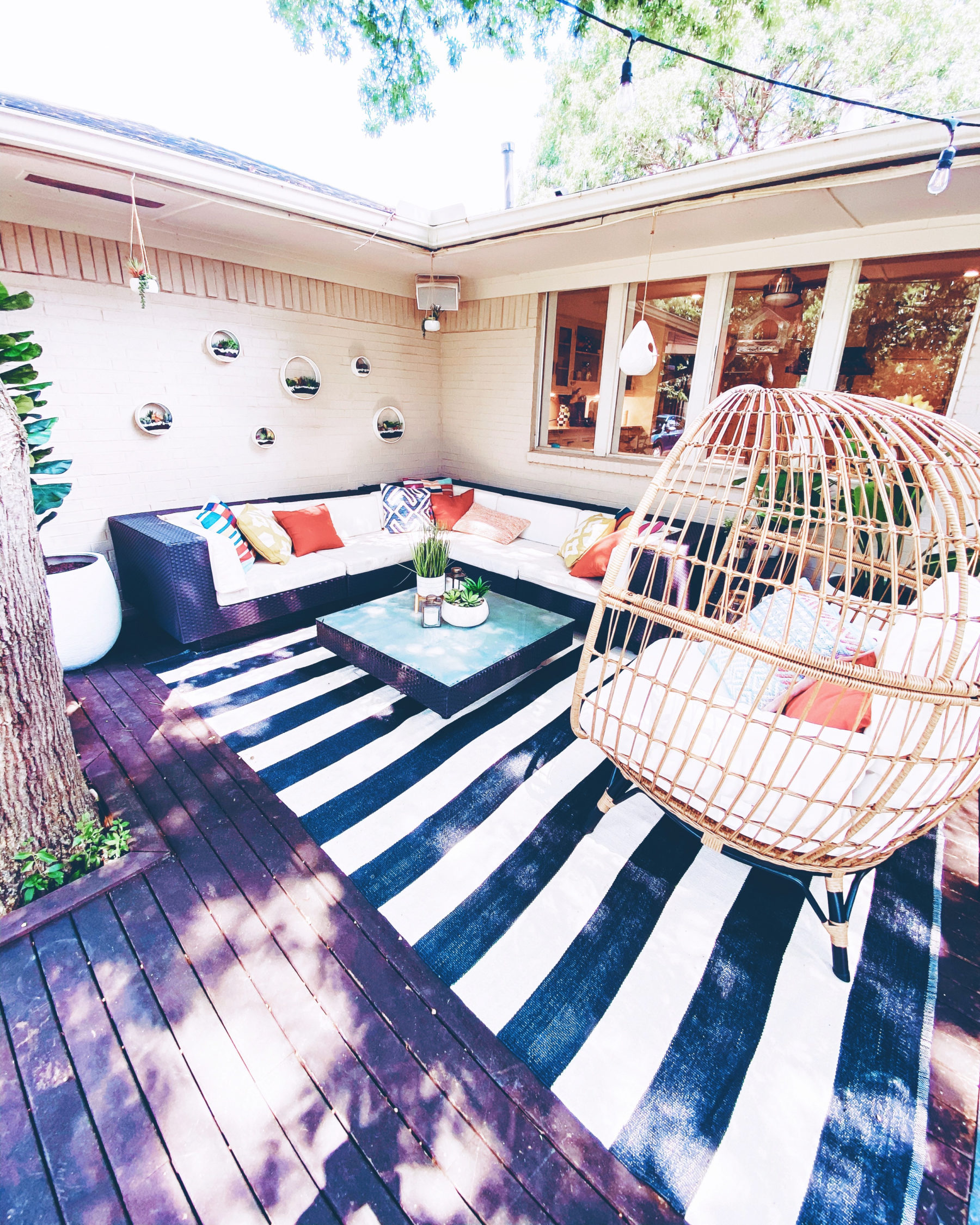 cute & little | dallas lifestyle blog | mid-century modern outdoor patio decorating ideas | egg chair, striped rug, brick wall planters, sectional | Mid Century Modern Backyard by popular Dallas lifestyle blog, Cute and Little: image of a backyard decorated with a Target Southport Patio Egg Chair, World Market Multicolor Ladder Stripe Indoor Outdoor Throw Pillow, World Market Blue And Ivory Geometric Indoor Outdoor Throw Pillow, World Market Arabesque Indoor Outdoor Throw Pillow, World Market Solid Outdoor Throw Pillow, World Market Woven Boucle Stripe Indoor Outdoor Lumbar Pillow, World Market Ceramic Sevilla Outdoor Planter, Boutique Rugs Douds Area Rug, West Elm Simple Wood Lanterns, Target Vickerman Artificial Potted Bird of Paradise Palm Tree, Pottery Barn Faux Potted Succulent in Ceramic Bowl, outdoor sectional couch and Target 12" x 10" Artificial Eucalyptus Plant Arrangement in Pot.