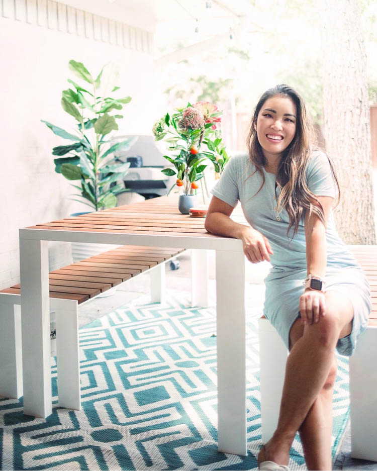 cute & little | dallas lifestyle blog | mid-century modern outdoor patio decorating ideas | egg chair | Mid Century Modern Backyard by popular Dallas lifestyle blog, Cute and Little: image of a woman sitting at a Design Within Reach Deneb Table with a Design Within Reach Deneb Bench that's next to a World Market Faux Fiddle-Leaf Fig Plant and Amazon LA JOLIE MUSE Tall Planters.