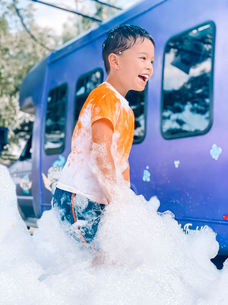 cute & little | dallas lifestyle blog | best social distancing birthday party ideas | bubble truck review | coupon discount promo code | Bubble Truck by popular Dallas lifestyle blog, Cute and Little: image of a boy playing in foamy bubbles created by the Bubble Truck.