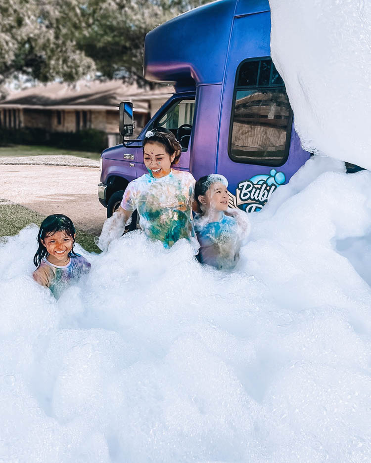 cute & little | dallas lifestyle blog | best social distancing birthday party ideas | bubble truck review | coupon discount promo code | Bubble Truck by popular Dallas lifestyle blog, Cute and Little: image of a mom and her two kids playing in foamy bubbles created by the Bubble Truck.
