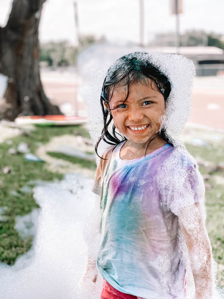 cute & little | dallas lifestyle blog | best social distancing birthday party ideas | bubble truck review | coupon discount promo code | Bubble Truck by popular Dallas lifestyle blog, Cute and Little: image of a girl playing in foamy bubbles created by the Bubble Truck.