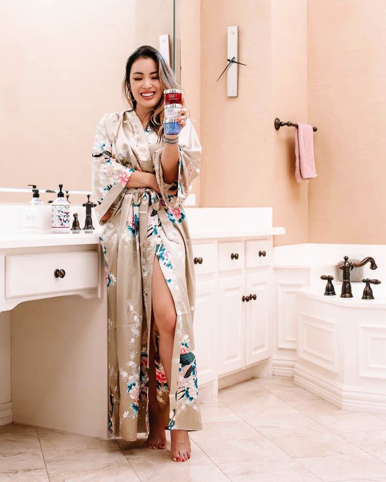 cute & little | dallas beauty skincare blog | anti-aging skincare routine for 30s | olay top drugstore skincare | Olay Skin Care by popular Dallas lifestyle blog, Cute and Little: image of a woman standing in her bathroom and wearing a OLDSHANGHAI Women's Kimono Robe while holding jars of Olay Regenerist Micro-Sculpting Cream Face Moisturizer, Olay Regenerist Brightening Vitamin C Facial Moisturizer, and Olay Regenerist Retinol 24 Night Facial Moisturizer.  