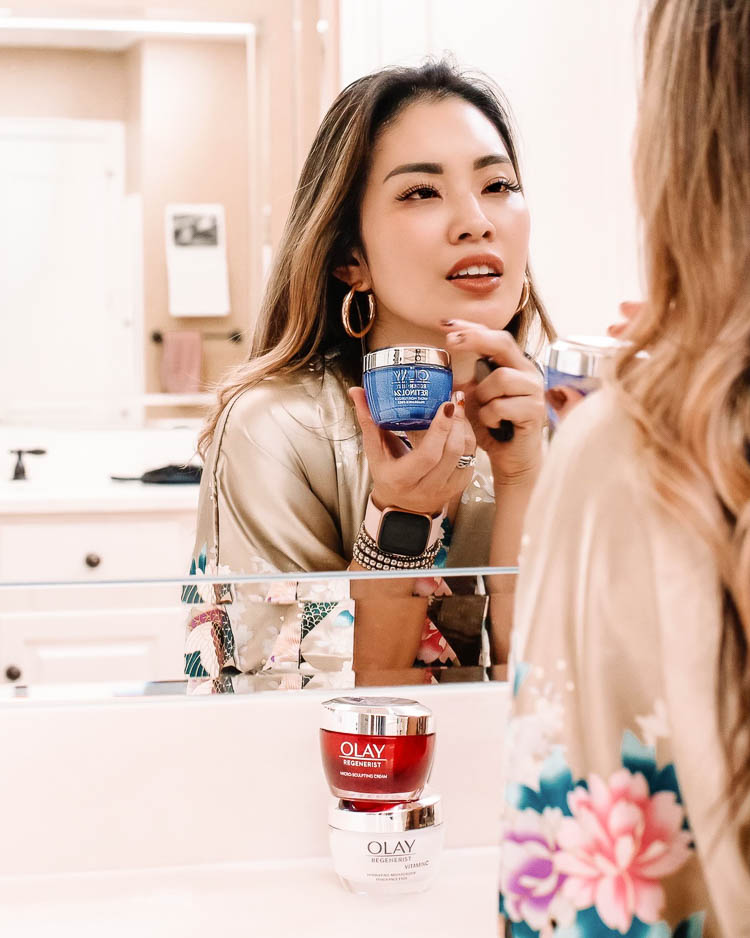 cute & little | dallas beauty skincare blog | anti-aging skincare routine for 30s | olay top drugstore skincare | olay retinol 24 vs micro-sculpting cream vs brightening + vitamin c hydrating moisturizer cream comparison |  Olay Skin Care by popular Dallas lifestyle blog, Cute and Little: image of a woman standing in her bathroom and wearing a OLDSHANGHAI Women's Kimono Robe while holding jars of Olay Regenerist Micro-Sculpting Cream Face Moisturizer, Olay Regenerist Brightening Vitamin C Facial Moisturizer, and Olay Regenerist Retinol 24 Night Facial Moisturizer. 