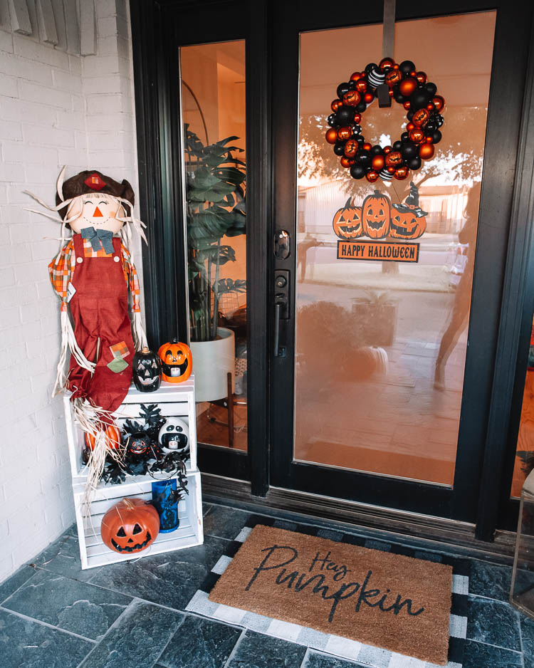 cute & little | dallas mom petite fashion blog | halloween front porch fall decor | walmart plus membership review |Walmart Halloween Decor by popular Dallas lifestyle blog, Cute and Little: image of a front porch decorated with a Walmart pumpkin wreath, pumpkin trio sign scarecrow, similar crates | similar light-up pumpkin similar 'hey pumpkin' doormat, buffalo check doormat giant spider, dog skeleton, and pumpkin pathway lights.