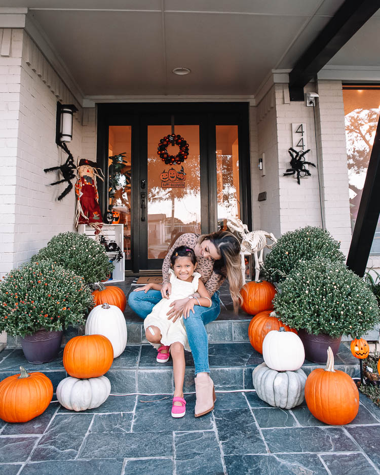 cute & little | dallas mom petite fashion blog | halloween front porch fall decor | walmart plus membership review |Walmart Halloween Decor by popular Dallas lifestyle blog, Cute and Little: image of a front porch decorated with a Walmart pumpkin wreath, pumpkin trio sign scarecrow, similar crates | similar light-up pumpkin similar 'hey pumpkin' doormat, buffalo check doormat giant spider, dog skeleton, and pumpkin pathway lights.