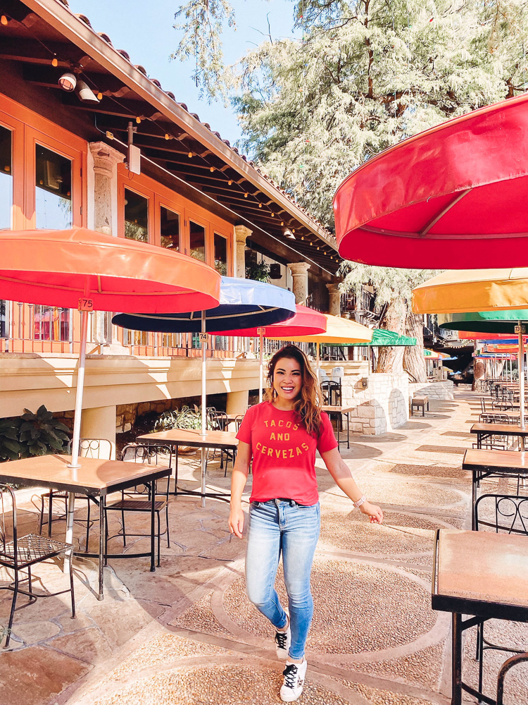 cute & little | dallas family travel blog | san antonio travel guide itinerary | riverwalk |San Antonio Vacation by popular Dallas travel blog, Cute and Little: image of a woman at The River's Edge Cafe and wearing a Fifth Sun Graphic T Shirt Red Tacos and Cerveza,AE Ne(x)t Level High Waisted Jegging, Golden Goose sneakers, and Dos Femmes Topo Loco Earrings.