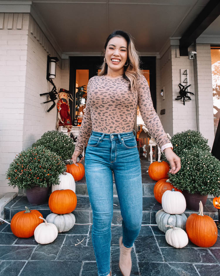 cute & little | dallas mom petite fashion blog | halloween front porch fall decor | walmart plus membership review | Cyber Monday Sales by popular Dallas petite fashion blog, Cute and Little: image of a woman standing on her front porch steps decorated with pumpkins and mums and wearing an Abercrombie and Fitch leopard bodysuit, Abercrombie and Fitch curvy jeans, and tan suede ankle boots. 
