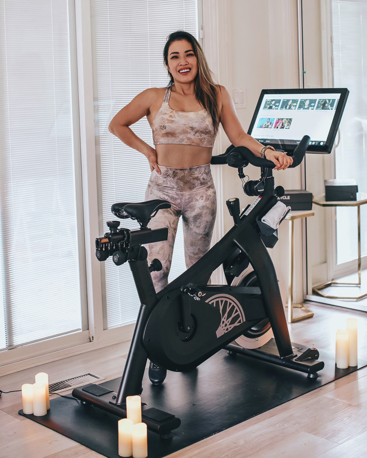 cute & little | dallas petite fashion fitness blog | soulcycle variis peleton at-home bike comparison review | SoulCycle At Home Bike by popular Dallas lifestyle blog, Cute and Little: image of a woman standing next to a SoulCycle At Home bike on a SoulCycle bike mat and wearing a pair of Athleta Elation Gilded Tight and a Athleta sports bra.  