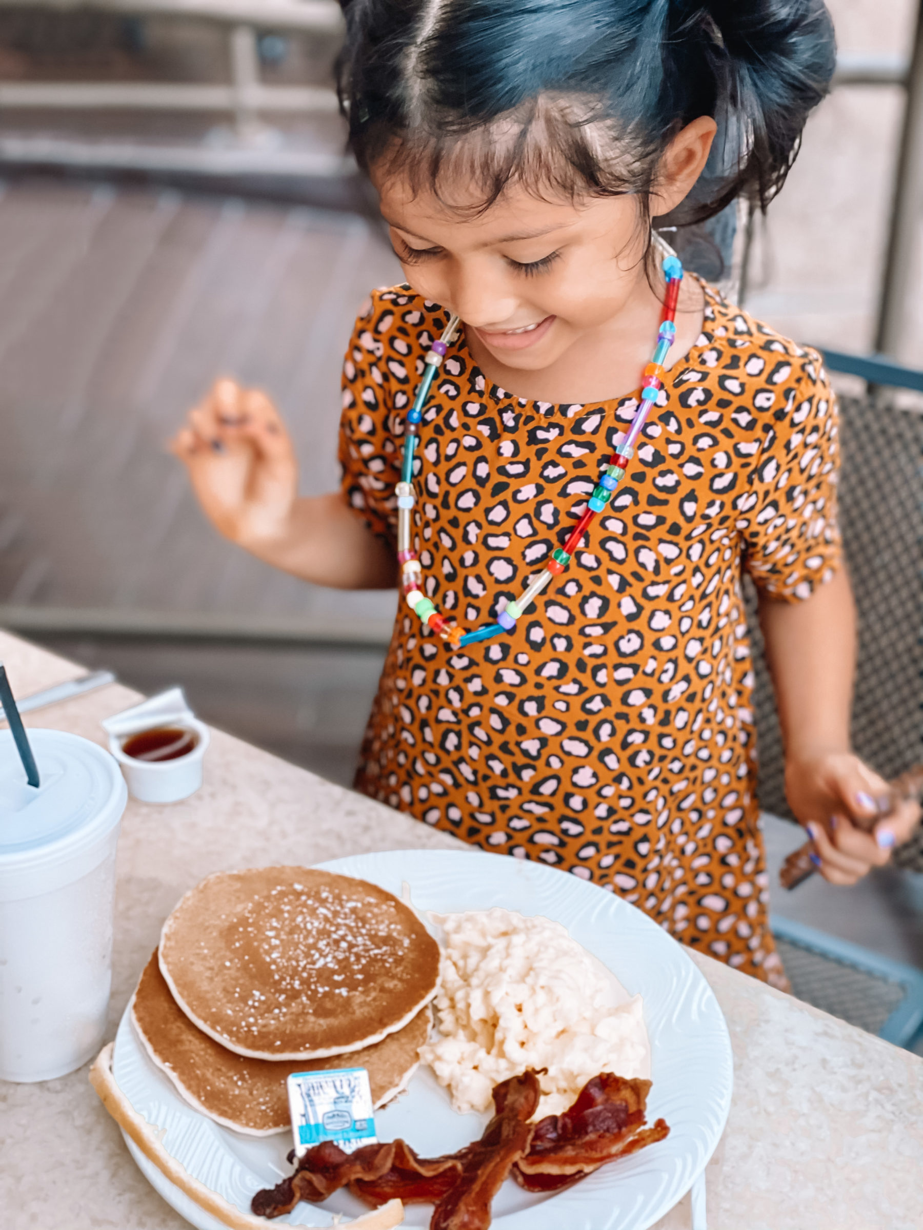 cute & little | dallas family travel blog | san antonio travel guide itinerary | riverwalk The River's Edge Cafe brunch |San Antonio Vacation by popular Dallas travel blog, Cute and Little: image of a girl wearing a leopard print dress and eating pancakes, eggs, and bacon at The River's Edge Cafe.