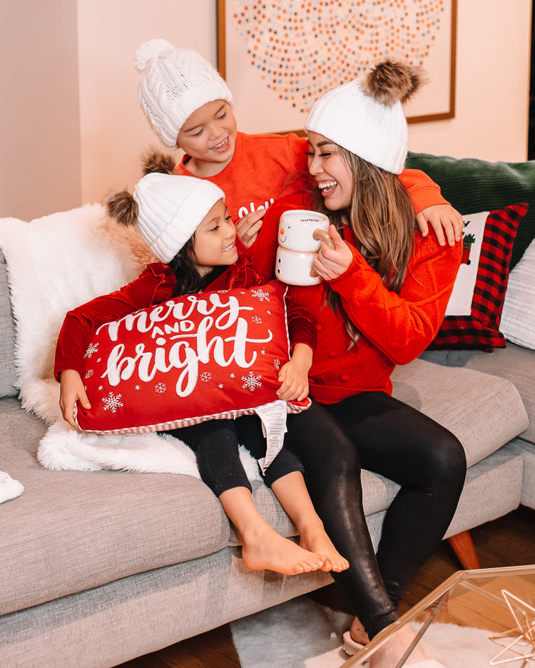 cute & little | dallas mom blog | holiday living room decor walmart |Walmart Holiday Decorations by popular Dallas life and style blog, Cute and Little: image of a mom and her two children sitting on a grey sectional couch and wearing red shirts, black leggings, and white beanies.. 