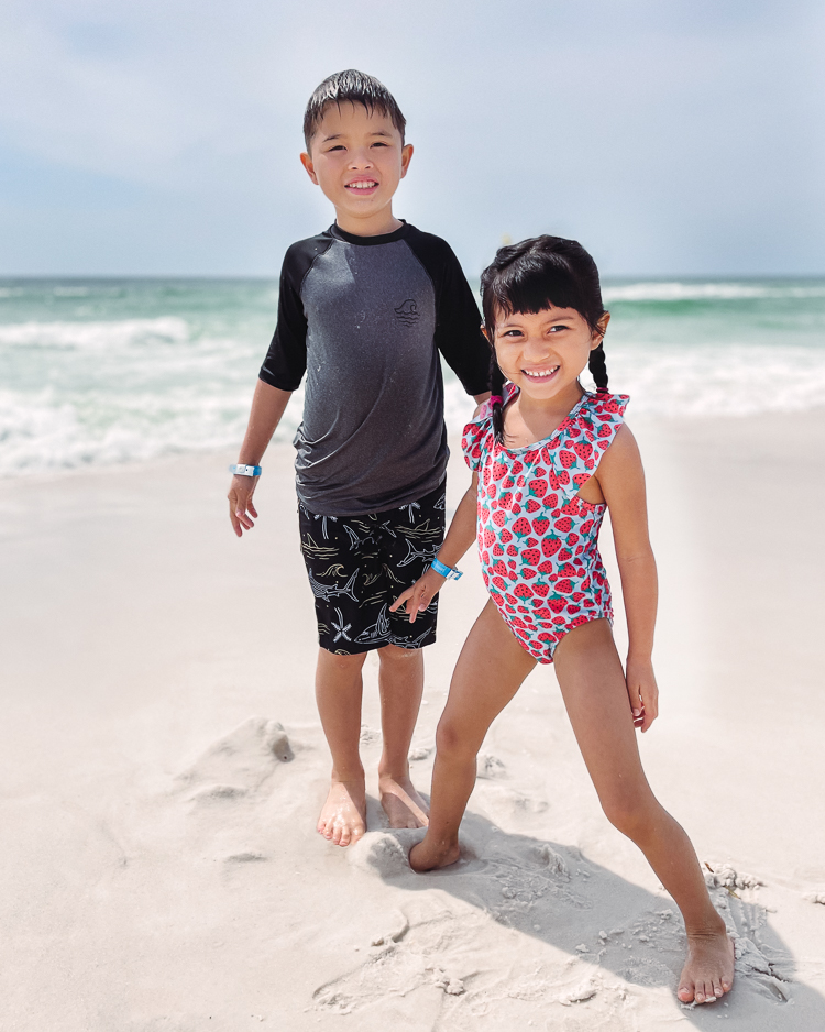 cute & little | dallas mom family travel blog | panama city beach 30a destin florida travel guide kids | holiday inn resort review |Panama City Beach by popular Dallas travel blog, Cute and Little: image of two young kids wearing a swimsuits and standing on a white sand beach. 