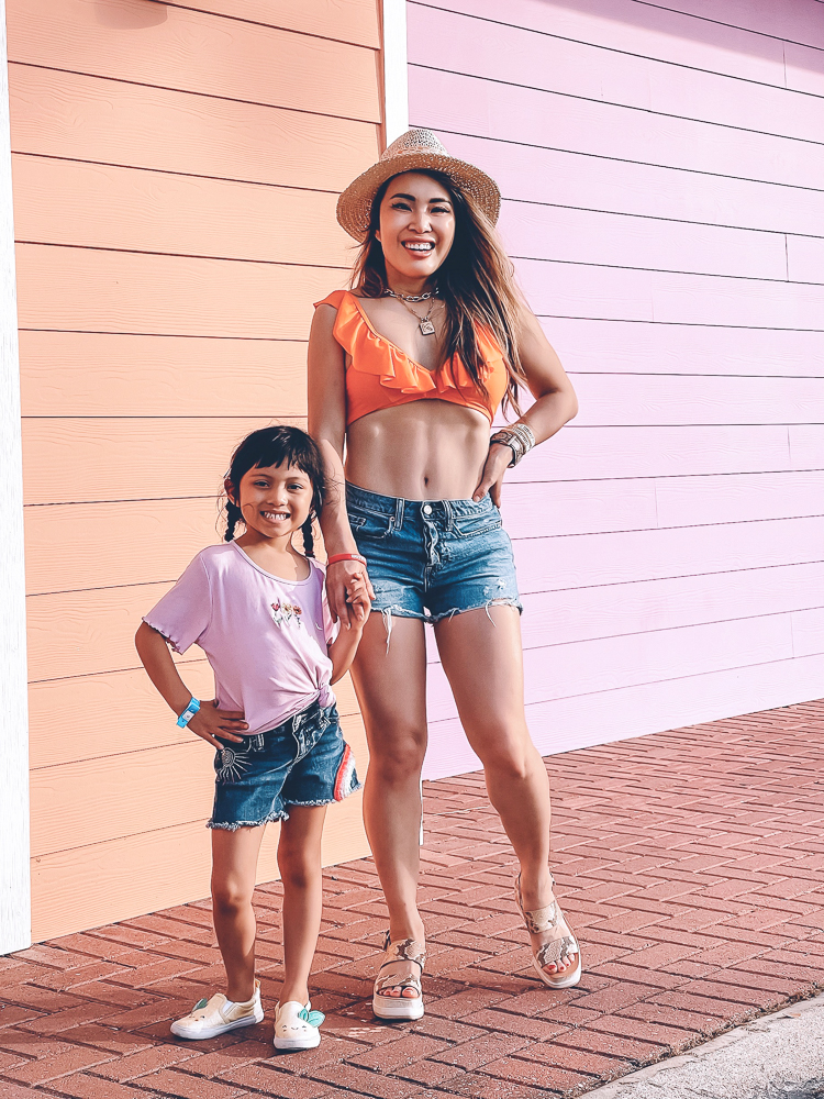 cute & little | dallas mom family travel blog | panama city beach 30a destin florida travel guide kids | amazon swimsuit pier park |Panama City Beach by popular Dallas travel blog, Cute and Little: image of a mom and daughter standing next to each other and wearing jean shorts, a pink t-shirt, an orange ruffle top swimsuit, and straw fedora hat. 