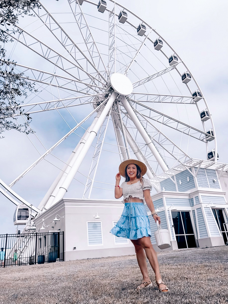 cute & little | dallas mom family travel blog | panama city beach 30a destin florida travel guide kids | amazon summer outfit pier park  |Panama City Beach by popular Dallas travel blog, Cute and Little: image of a woman standing next to a ferris wheel and wearing an Amazon polka dot crop top and ruffle denim skirt with espadrille sandals. 