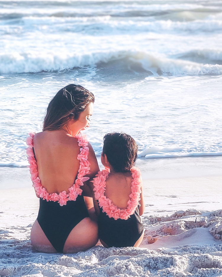 cute & little | dallas mom family travel blog | panama city beach 30a destin florida travel guide kids |Panama City Beach by popular Dallas travel blog, Cute and Little: image of a mom and daughter sitting next to each other on a white sand beach and wearing matching flower applique swimsuits. 