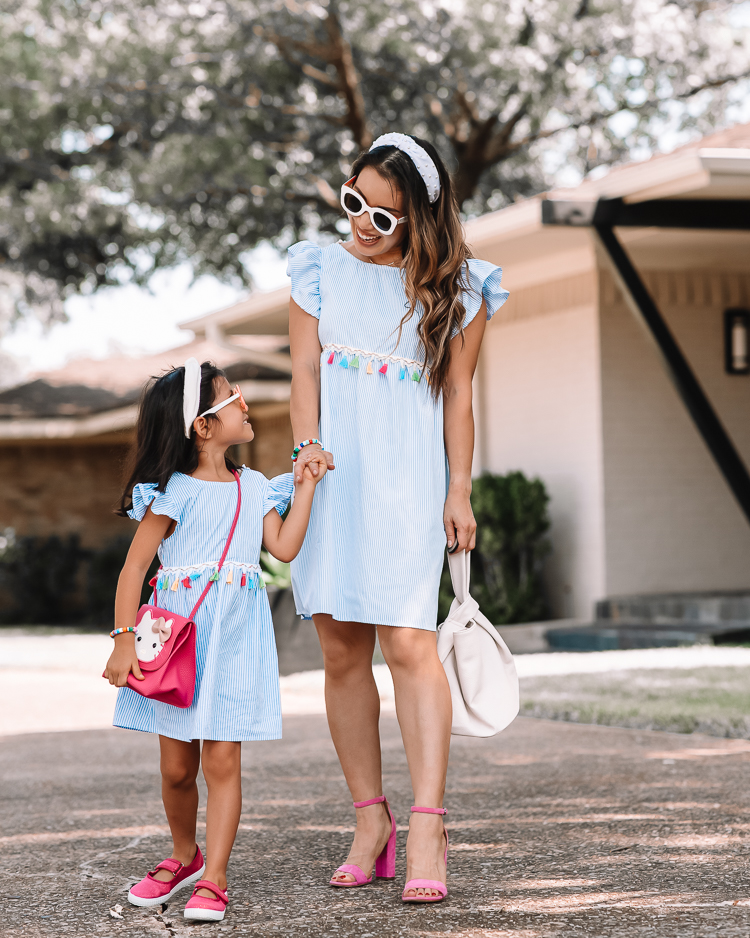 cute & little | dallas mom petite fashion blog | mom daughter matching spring summer dress outfits |Mommy and Me Outfits by popular Dallas petite fashion blog, Cute and Little: image of a mom and her daughter standing outside and wearing matching blue and white stripe tassel dresses, white knot headbands, sunglasses, and pink shoes. 