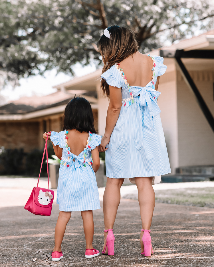 cute & little | dallas mom petite fashion blog | mom daughter matching spring summer dress outfits |Mommy and Me Outfits by popular Dallas petite fashion blog, Cute and Little: image of a mom and her daughter standing outside and wearing matching blue and white stripe tassel dresses, white knot headbands, sunglasses, and pink shoes. 