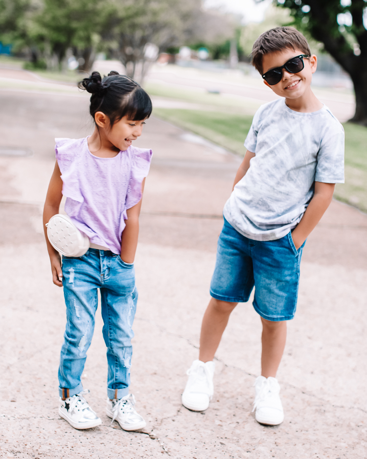 cute & little | dallas mom family blog | kidpik review | best kids style box |KidPik Box by popular Dallas petite fashion blog, Cute and Little: image of a young boy and girl standing together outside and holding hands and wearing a purple eyelet flutter sleeve shirt, distressed jeans, white sneakers, studded white belt bag, grey tie dye shirt, jean shorts, white sneakers, and black sunglasses. 