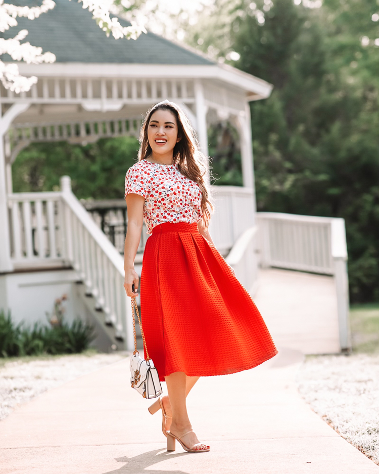 cute & little | dallas mom petite fashion blog | cherry tee, red retro midi skirt | mothers day gift guide 2021 |Mother's Day Gifts by popular Dallas life and style blog, Cute and Little: image of a woman standing in front of a white gazebo and wearing a LOFT Cherry Crew Tee, red pleated skirt, Dolce Vita 'Noles', white knot headband, and Fitbit 'Versa 2'  w/ leopard Spark*l Band