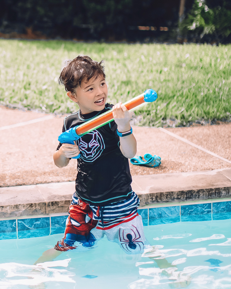 cute & little | dallas mom family travel blog | walmart plus review | backyard pool day must-haves | Pool Day by popular Dallas lifestyle blog, Cute and Little: image of a young boy standing in a swimming pool and holding a squirt gun.