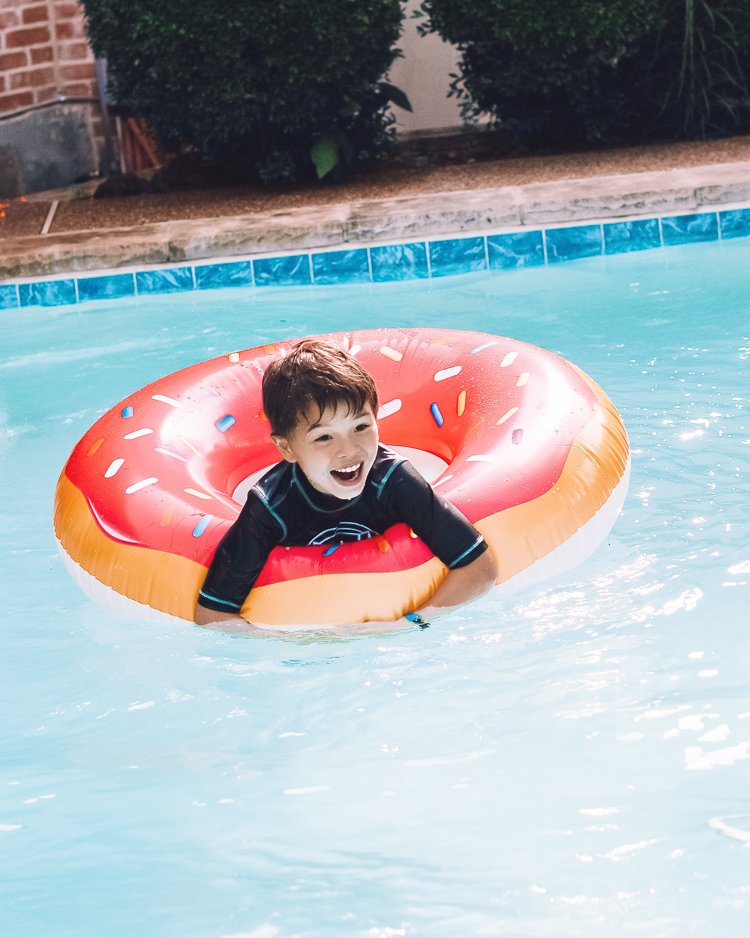 cute & little | dallas mom family travel blog | walmart plus review | backyard pool day must-haves | Pool Day by popular Dallas lifestyle blog, Cute and Little: image of a boy floating in a donut pool float in a swimming pool. 
