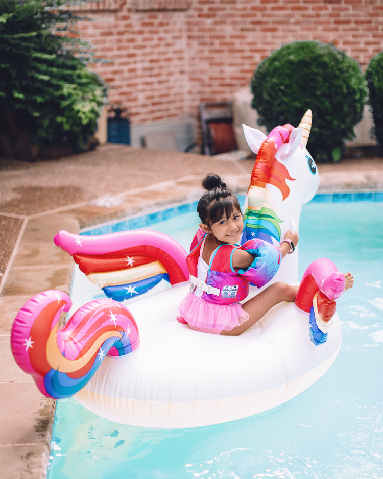 cute & little | dallas mom family travel blog | walmart plus review | backyard pool day must-haves | Pool Day by popular Dallas lifestyle blog, Cute and Little: image of a girl sitting in a unicorn pool float in a swimming pool.