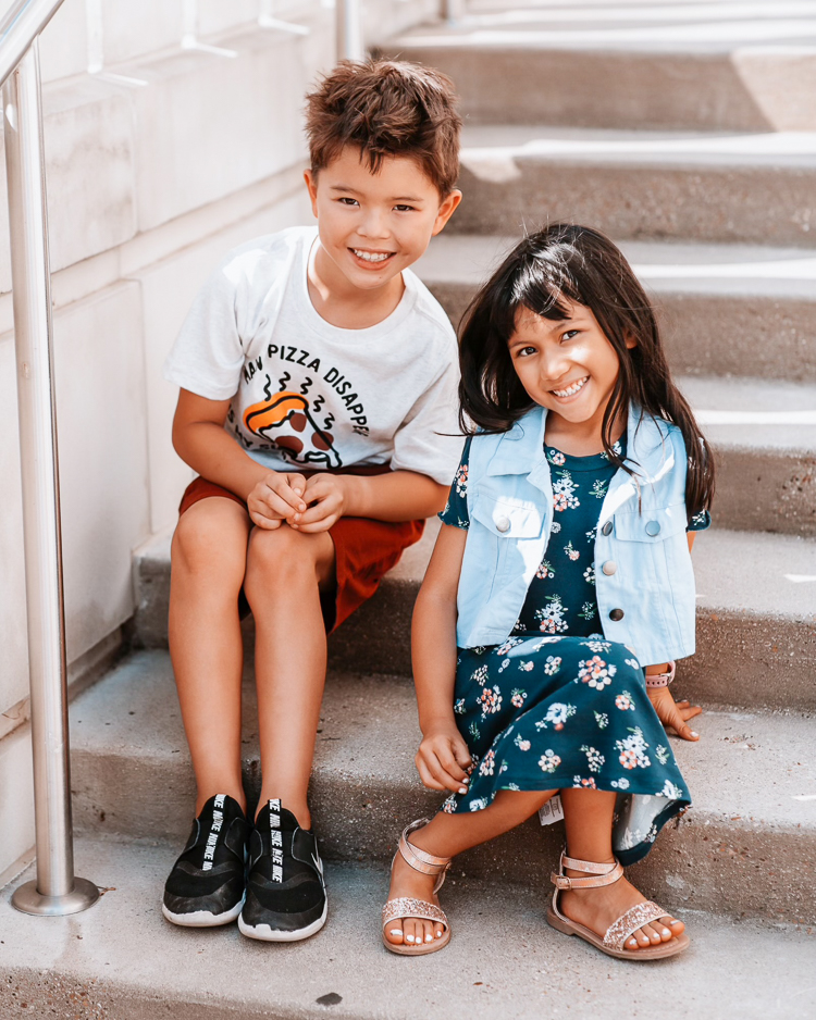 cute & little | dallas petite fashion blog | back to school outfits jcpenney |  School Routine by popular Dallas motherhood blog, Cute and Little: image of a brother and sister sitting on some cement steps and wearing a pizza graphic t-shirt, red shorts, black Nike sneakers, floral print dress, gold strap sandals, and denim dress. 