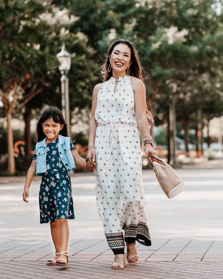 cute & little | dallas petite fashion blog | back to school and back to work outfits jcpenney | School Routine by popular Dallas motherhood blog, Cute and Little: image of a mom standing outside with her daughter and wearing a white sleeveless jumpsuit, white strap block heel sandals, floral print dress, gold strap sandals, and denim vest. 