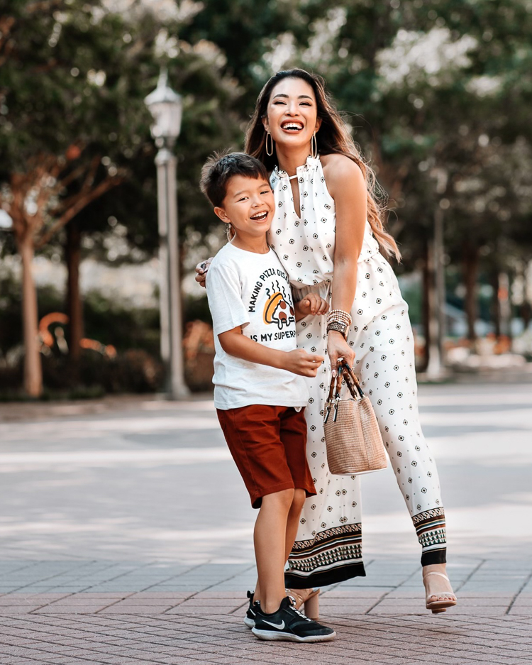 cute & little | dallas petite fashion blog | back to school and back to work outfits jcpenney | School Routine by popular Dallas motherhood blog, Cute and Little: image of a mom standing outside with her son and wearing a white sleeveless jumpsuit, white strap block heel sandals, pizza graphic t-shirt, red shorts and black Nike sneakers. 