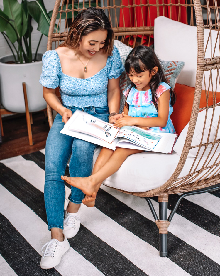 cute & little | dallas mom blogger | Artkive review | parenting de-clutter tip | how to store kids' artwork | Kids Artwork by popular Dallas motherhood blog, Cute and Little: image of a mom and her young daughter sitting in a rattan egg chair and looking art a book filled with artwork. 