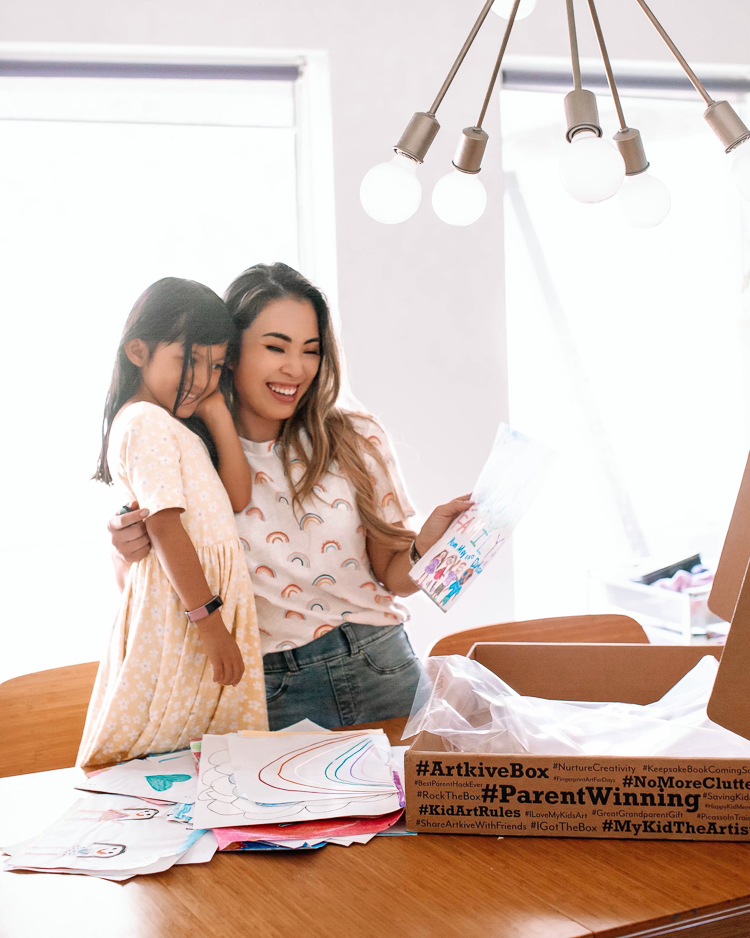cute & little | dallas mom blogger | Artkive review | parenting de-clutter tip | how to store kids' artwork | Kids Artwork by popular Dallas motherhood blog, Cute and Little: image of a mom hugging her daughter and looking at a picture that the daughter drew. 
