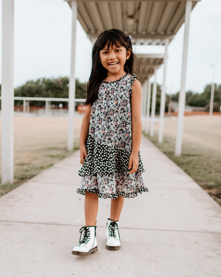 cute & little | dallas petite fashion mom blogger | toddler girl black floral dress white doc marten combat boots | fall outfit | Doc Martens Combat Boots by popular Dallas petite fashion blog, Cute and Little: image of a young girl standing outside and wearing a sleeveless black and white floral print midi dress with white Doc Martens combat boots. 